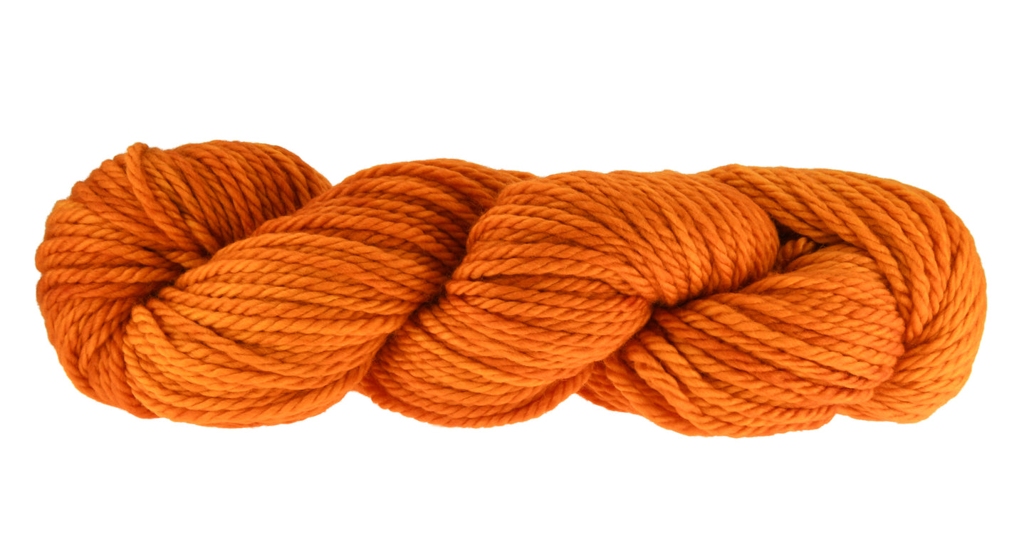 A twisted skein of Barn Yarn bulky weight hand-dyed yarn in colorway Pumpkin Orange in a bold, glowing orange shade, perfect for knitting and crochet projects with autumn warmth.