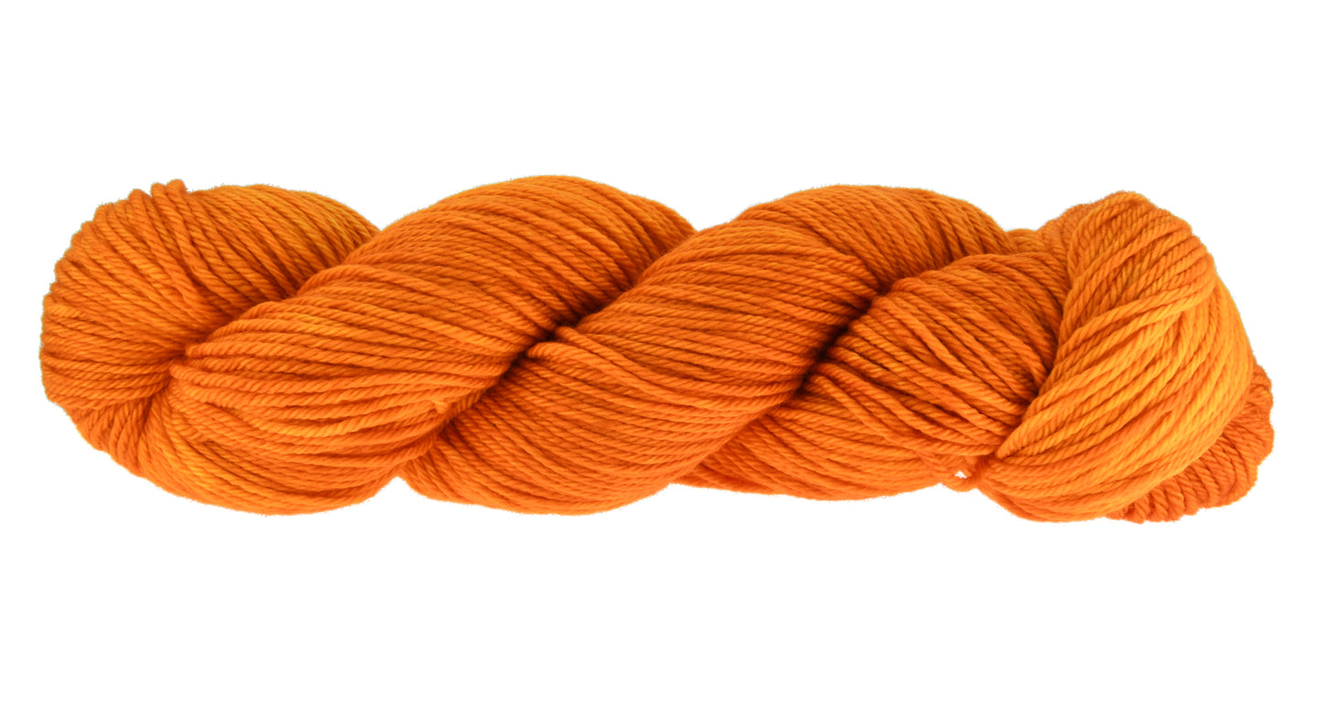 A twisted skein of Barn Yarn merino/cashmere/nylon fingering weight hand-dyed yarn in colorway Pumpkin Orange in a bold, glowing orange shade, perfect for knitting and crochet projects with autumn warmth.