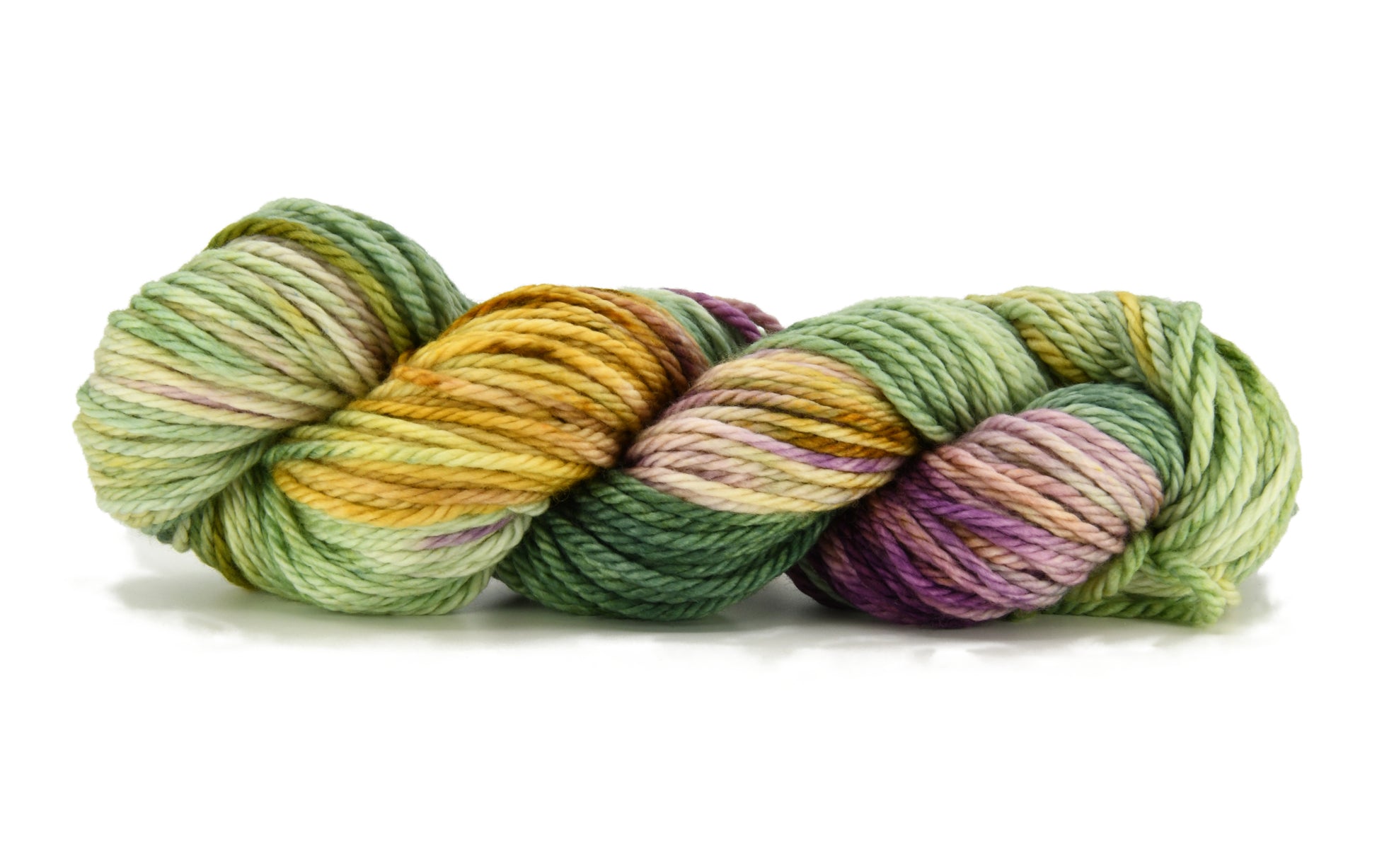 A twisted skein of Barn Yarn hand-dyed bulky weight yarn in colorway Pistachio, soft green shades with creamy toffee and purple undertones, perfect for fresh and playful knitting and crochet projects.