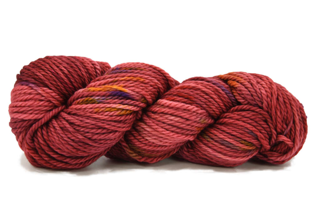 A twisted skein of Barn Yarn hand-dyed bulky weight yarn in colorway Smitten - reddish cinnamon with flecks of purple, orange, brown and red undertones, perfect for cozy knitting and crochet projects.