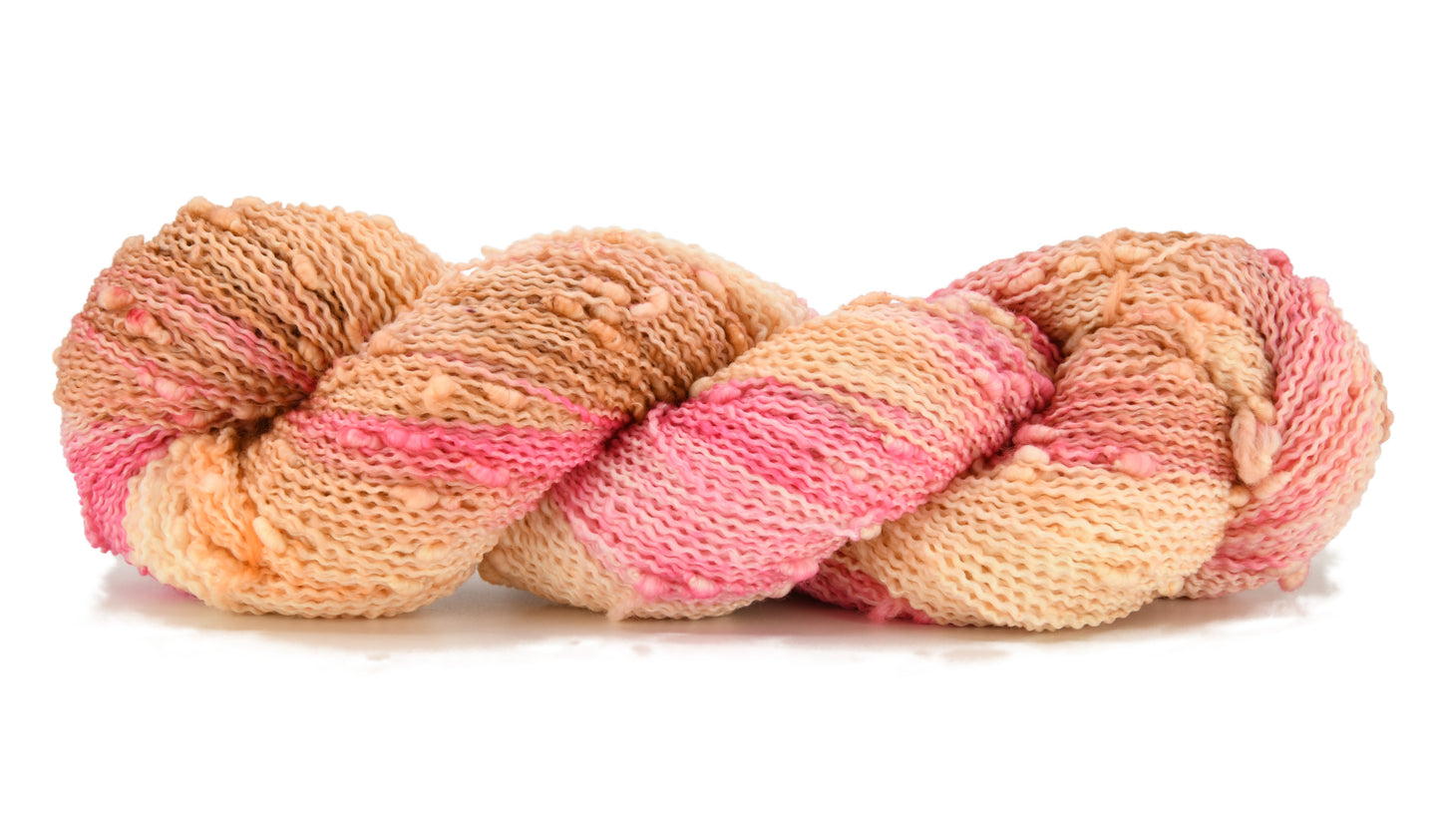 A twisted skein of Barn Yarn hand-dyed slub yarn in colorway Poolside Popsicle featuring bright strawberry pink, vanilla and chocolate sprinkles, perfect for knitting and crochet projects.