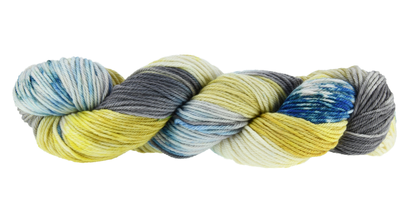 A twisted skein of Barn Yarn hand-dyed worsted weight yarn in colorway Beehive featuring golden yellow, soft gray and blue tones, perfect for warm and vibrant knitting and crochet projects.