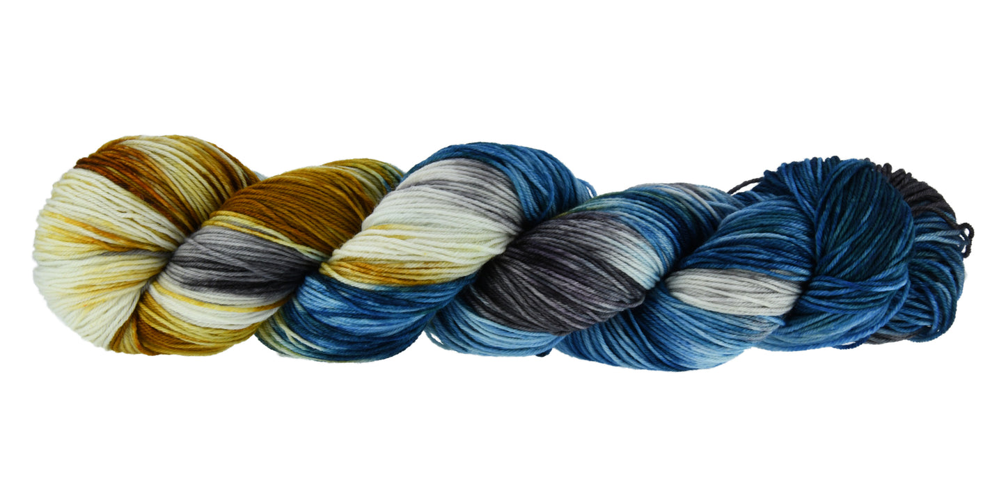 Barn-Yarn-Smoky-Mountain-fingering-weight-hand-dyed-yarn—twisted-hank-in-dark-and-bright-blue-with-toffee-and-gray-tones-evoking-the-texture-and-colors-of-mountain-landscapes.