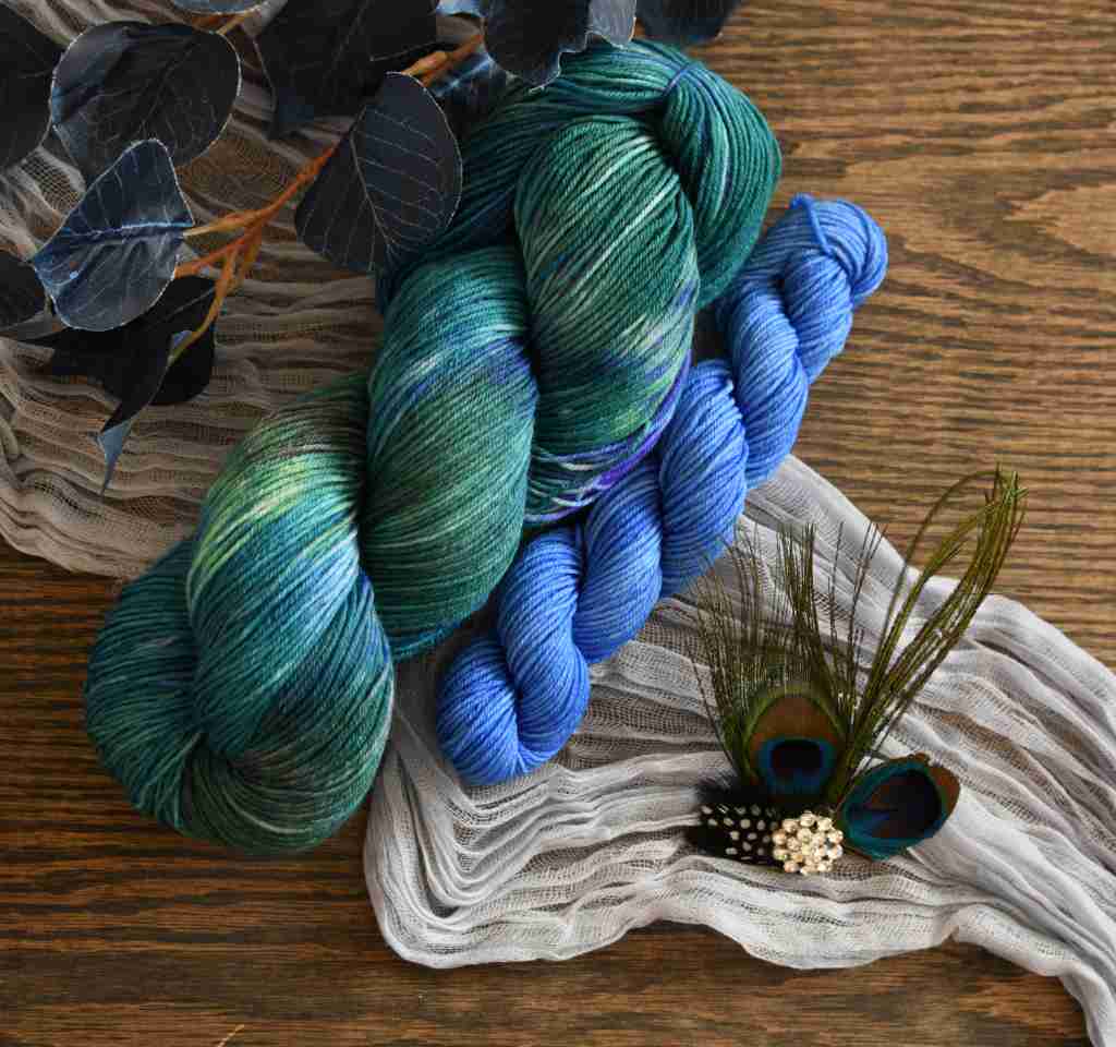 Twisted skeins of Barn Yarn hand-dyed blue mini and coordinating yarn in colorway Play the Peacock-vibrant teal, emerald green, rich blue inspired by the colors of a peacock’s feathers.