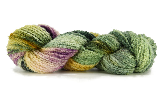 A twisted skein of Barn Yarn hand-dyed boucle DK weight yarn in colorway Pistachio, soft green shades with creamy toffee and purple undertones, perfect for fresh and playful knitting and crochet projects.