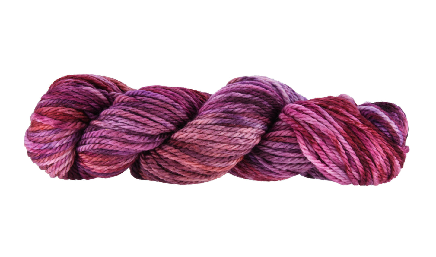 A twisted skein of Barn Yarn hand-dyed bulky weight yarn in colorway Feelin’ Berry Glam! featuring vibrant berry tones with purple, pink, and jewel-like shades, perfect for stylish knitting and crochet projects.
