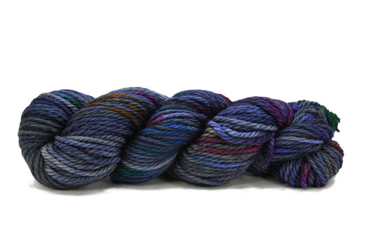 A twisted skein of Barn Yarn hand-dyed bulky weight yarn in colorway Hallucination - deep bluish purple with undertones of magenta, gray, rust, and blue, ideal for knitting and crochet.