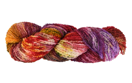 A twisted hank of Reykjavik Hot Spot hand-dyed boucle DK weight yarn showing a lively mix of red, orange, salmon pink, sage green, and deep aubergine, perfect for vibrant handmade creations.