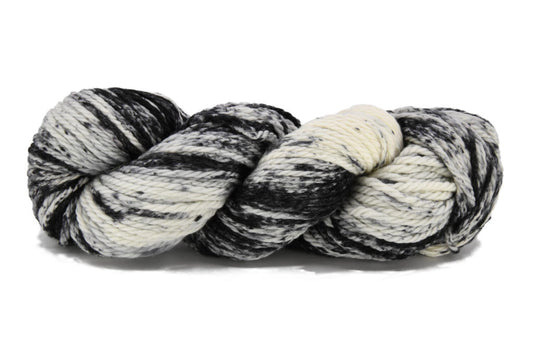 A twisted skein of Barn Yarn hand-dyed bulky weight yarn in colorway Timeless - cream with tonal black and black speckles, perfect for cozy and modern knit and crochet projects.