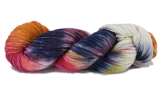A twisted skein of Barn Yarn hand-dyed fingering weight yarn in colorway Galaxy Nebula featuring deep purple, blue, and fiery orange with bursts of magenta and starry white, perfect for celestial knitting or crochet projects.