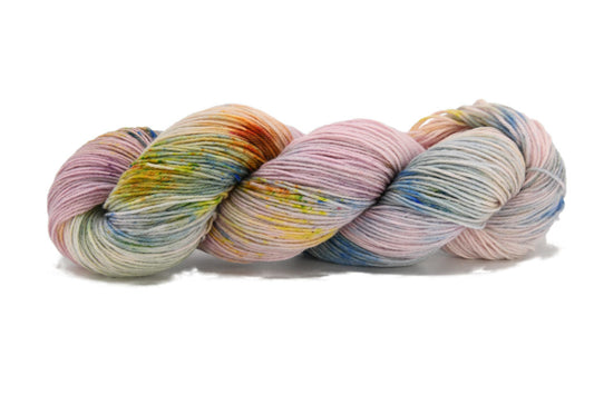 A twisted skein of Barn Yarn Snowflake 2 fingering weight hand-dyed yarn in light pink and blue with orange, yellow, and green speckles, made sustainably from recycled dye.