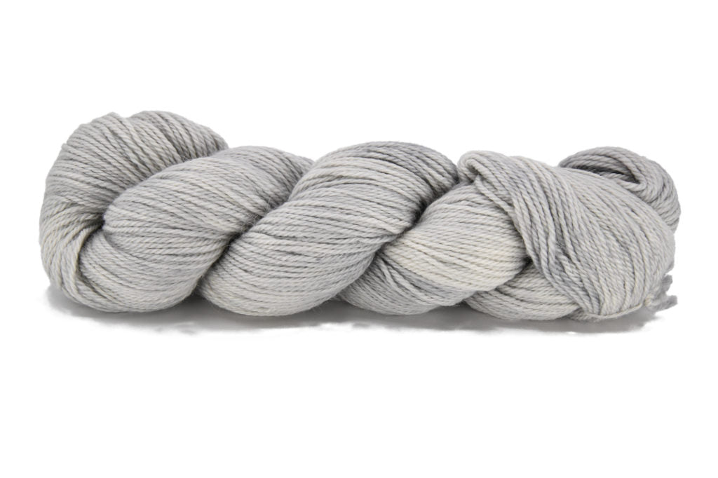 A twisted skein of Barn Yarn hand-dyed sport weight alpaca yarn in colorway Silver Bells -silvery-gray tones, perfect for soft and elegant knitting or crochet projects. 