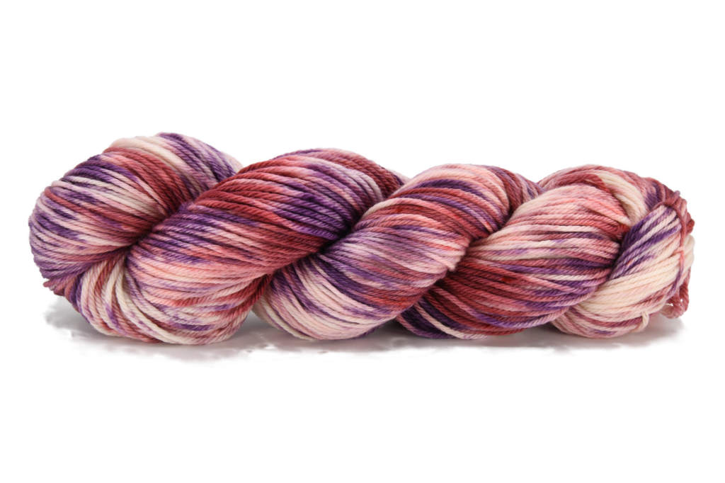 A twisted skein of Barn Yarn hand-dyed worsted weight yarn in colorway Very Berry - saturated berry tones of pink, purple and plum, perfect for cozy knitting and crochet projects.