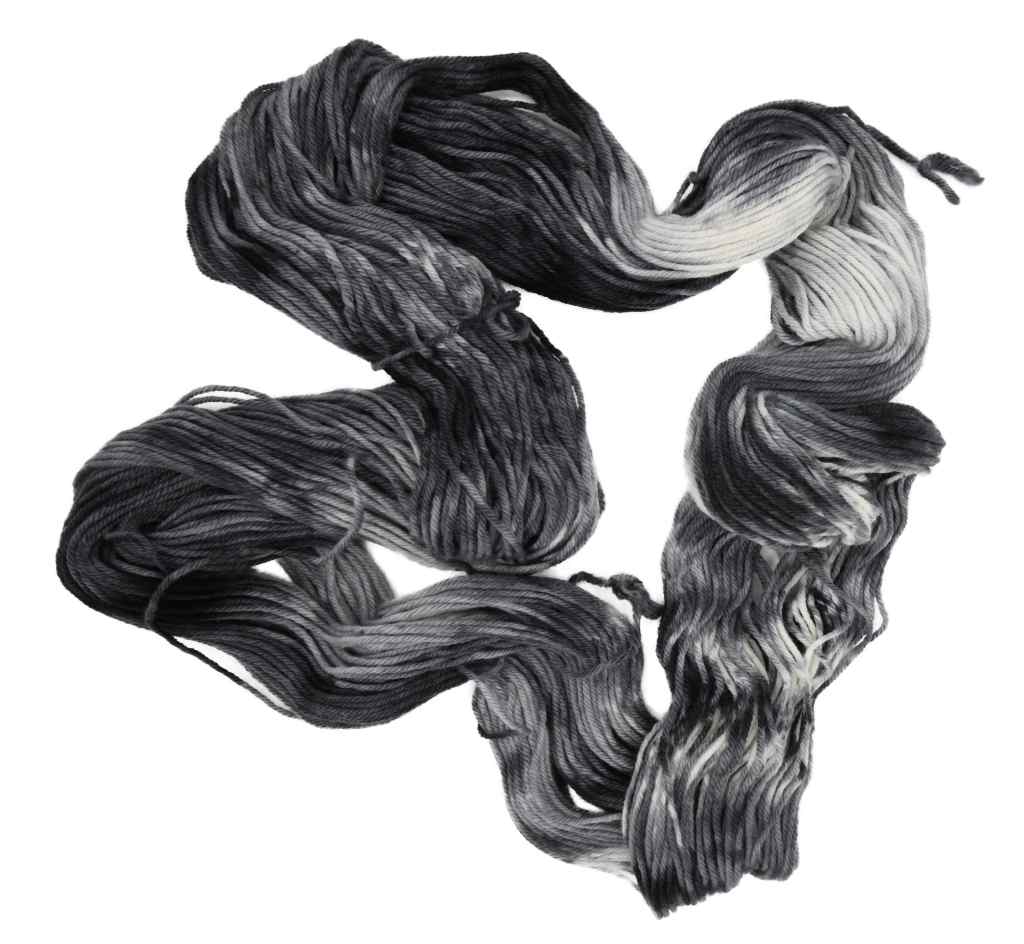 An unfolded skein of Barn Yarn hand-dyed worsted weight yarn in Colorway Storm - black, gray, and cream, evoking the moody tones of a passing storm - perfect for knit and crochet projects